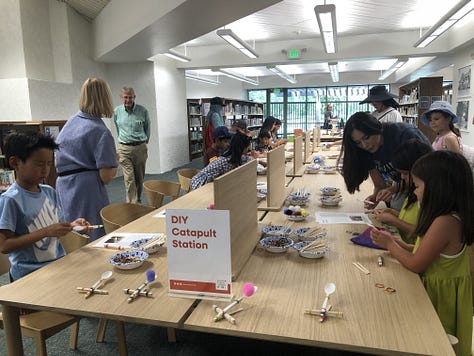 Adults and children in a public library borwworing, browsing, returning  books 