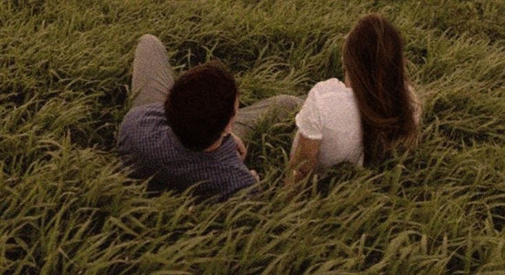 This may contain: two people are sitting in the tall grass