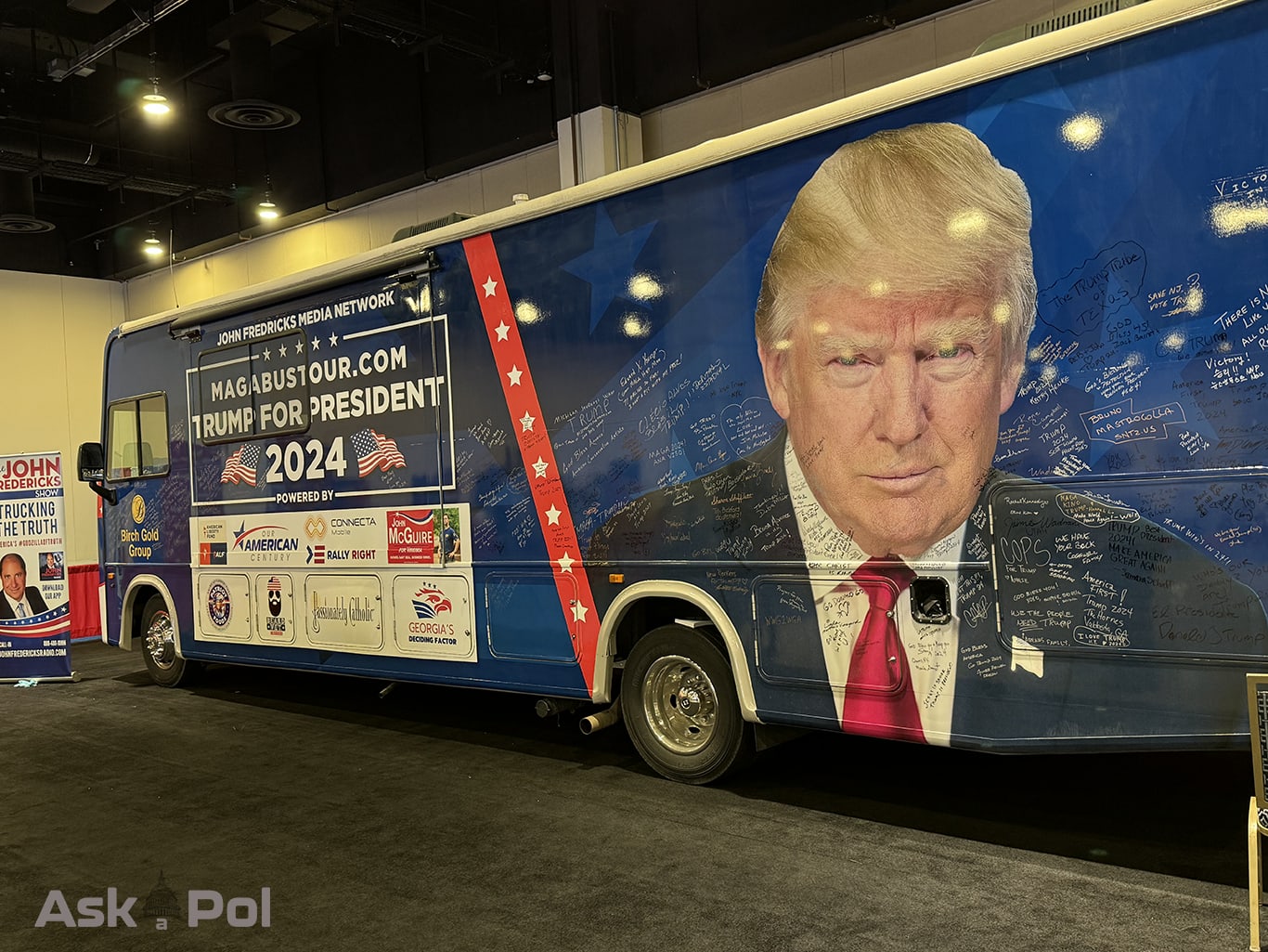 A bus with Prersident Donald Trump's face on it is parked indoors, it reads Trump for PResident 2024. Photo: Matt Laslo © www.askapolpoilitics.com