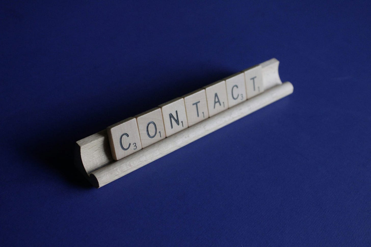 Scrabble rack with the letters spelling, "Contact", set on a blue background