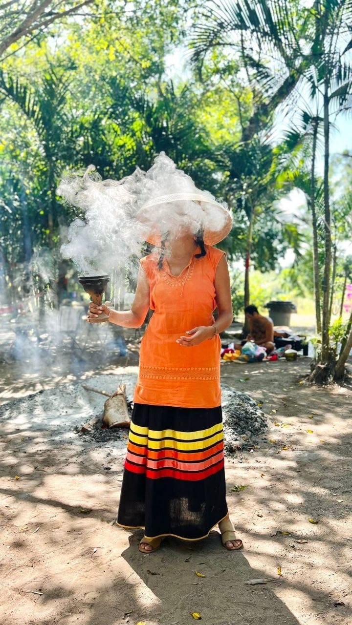 Copal smoke completely veils the face of a practitioner in ceremonial dress standing in a sunlit clearing