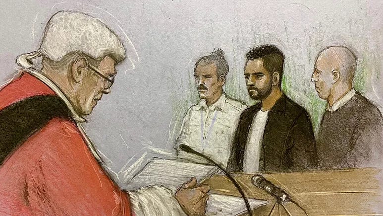 Homem vestido com roupa vermelha lê um documento em um microfone para tres outros homens que estao ao fundo