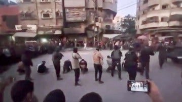 Videograb allegedly showing a Hamas firing squad executing collaborators, with people kneeling on the ground and others standing, while a person in the foreground records the scene on a phone.