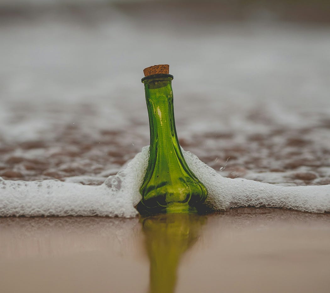green glass bottle with a cork in it and note inside, washed up on a beach (writer portfolio how to)