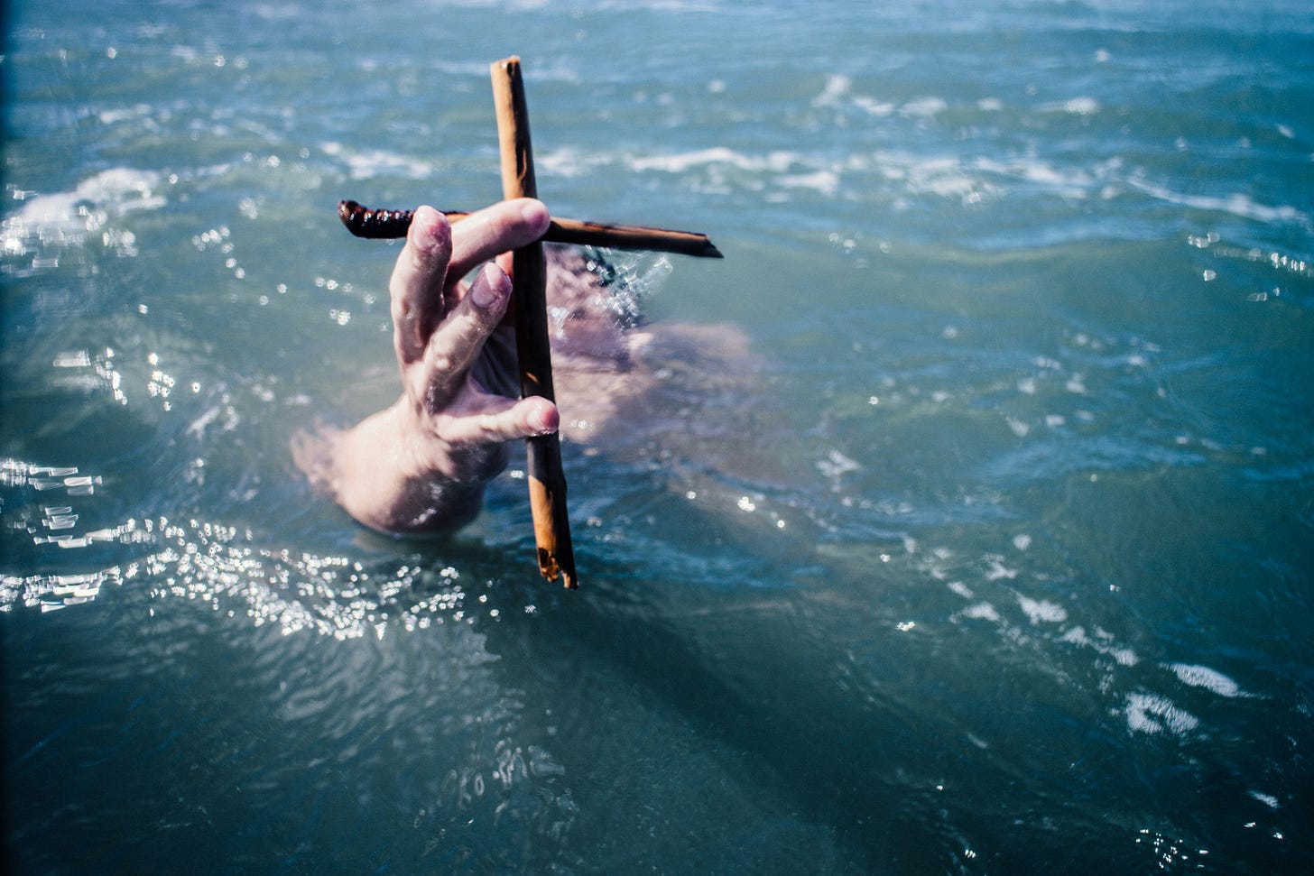 person underwater holding up brown wooden cross above the surface at daytime