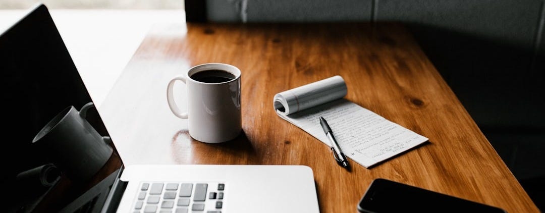 MacBook Pro, white ceramic mug,and black smartphone on table