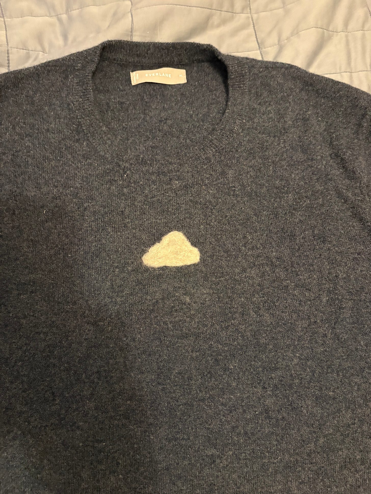 A dark gray cashmere sweater with a little white cloud patch covering a moth hole