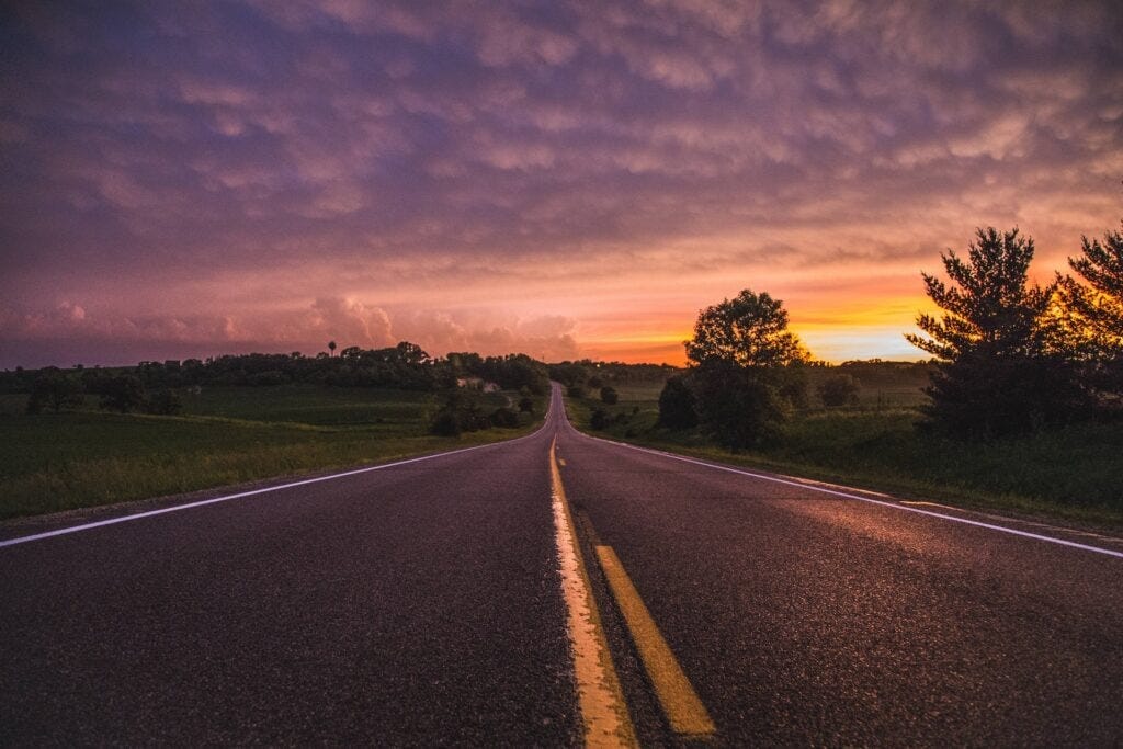 An empty road in between grass field at sunrise