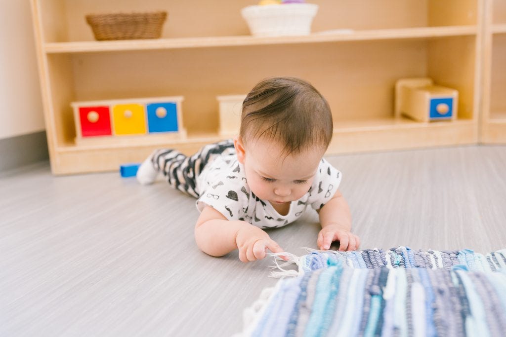 Baby doing tummy time on the floor of a Montessori Nido classroom, reaching toward a woven rug Big feelings