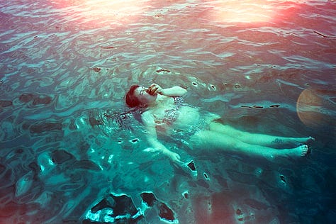 top row, left to right: nat lies face down in bed without a shirt on; their overgrown undercut is visible. a white liquid dissipates in green water under a dock. a bouquet of dried hydrangeas hang on a closet door. bottom row: the sun rises over a bedroom in cape may, nj. on blue film stock, nat floats in the lake and eats a peach. a pink bmw convertible is parked outside ike’s auto shop.