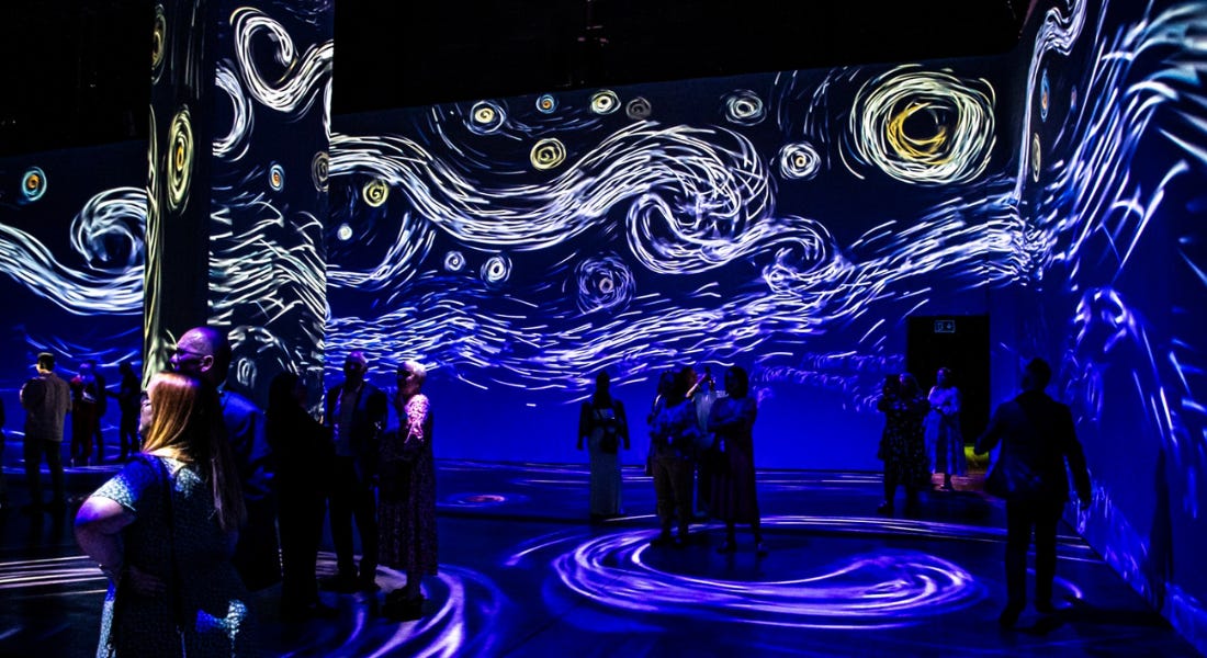 A dark blue exhibition room with swirling patterns and people stood around