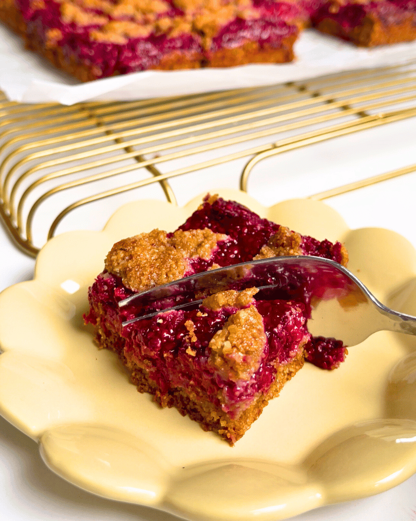 a slice of raspberry jam oat bars on a yellow plate with a fork cutting into it