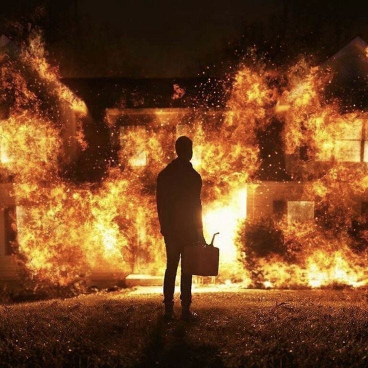 This may contain: a man holding a briefcase standing in front of a house on fire with flames behind him