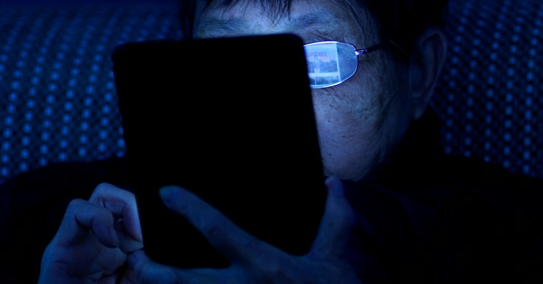 a man sitting in a dark room using a tablet computer