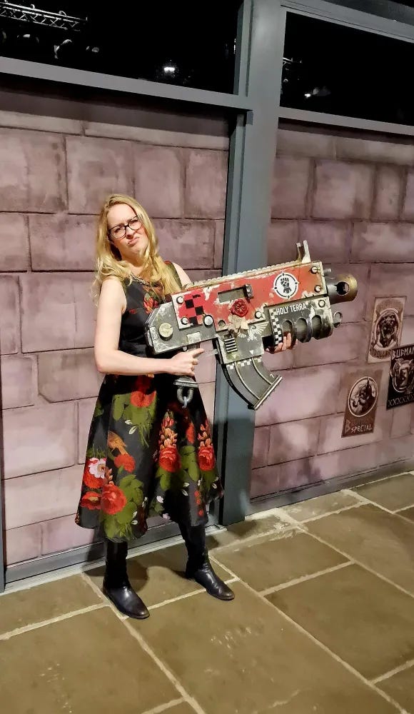 Victoria wields a giant bolt gun and wears a black and red floral dress Victoria wields a giant bolt gun and wears a black and red floral dress