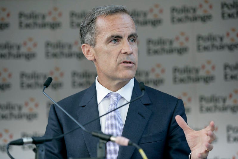 A man, Mark Carney, stands at a podium in front of a microphone and rasies his hands while speaking. A man, Mark Carney, stands at a podium in front of a microphone and rasies his hands while speaking.