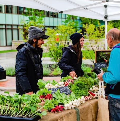 vendors and customers at a stand at a farmers market