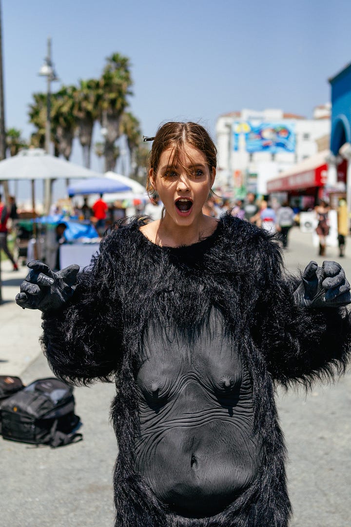 Barbara Palvin and Ashley Hart on set, laughing and posing with a gorilla suit—pulling it on, peeling it off, and mixing fashion with absurdity during the Mambo Goddess campaign shoot.