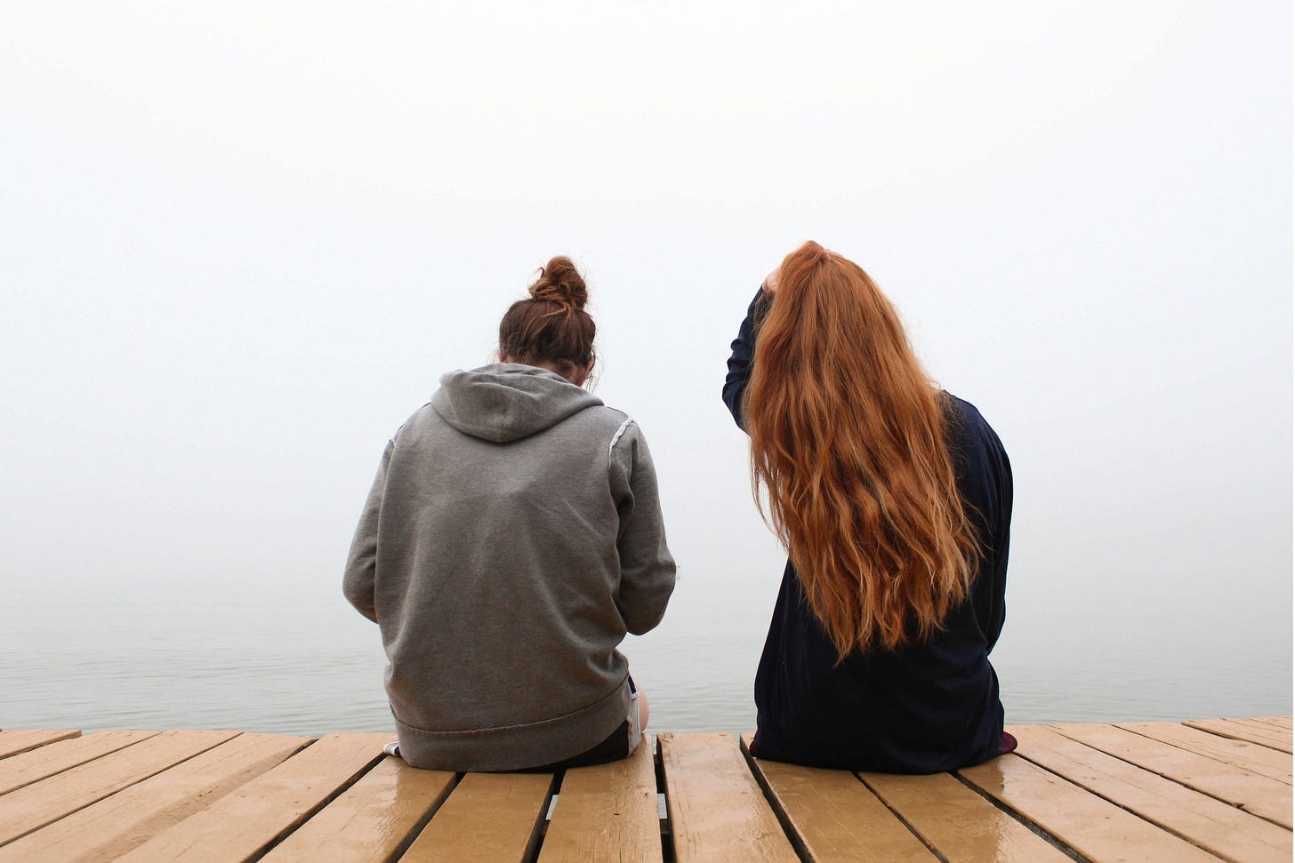 Two women sitting on a jetty overlooking the water with their backs to the camera. Photo by KaLisa Veer via Unsplash.