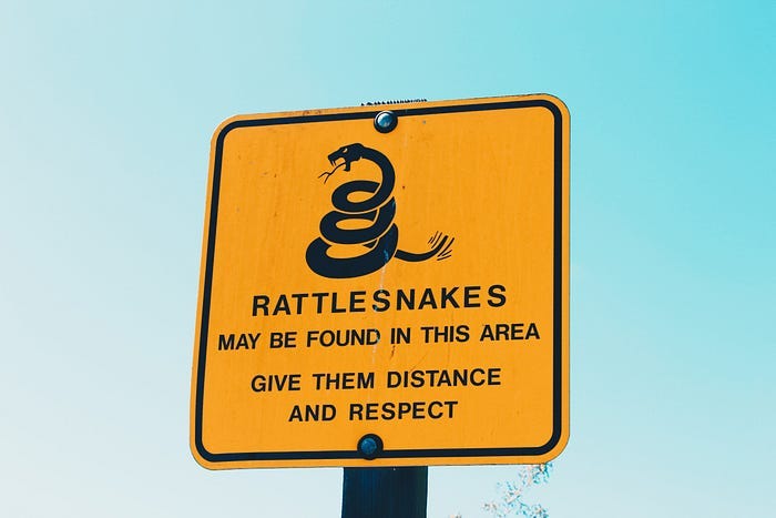A yellow hazard sign: “Rattlesnakes may be found in this area. Give them distance and respect.” A yellow hazard sign: “Rattlesnakes may be found in this area. Give them distance and respect.”