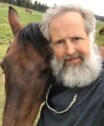 man with white hair and full beard embracing head of brown horse