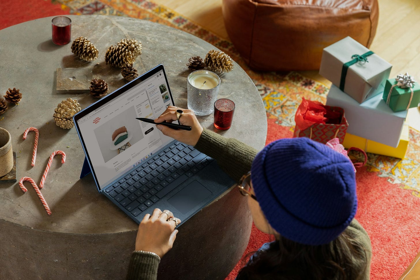 A person wearing a blue beanie shops online from a laptop surrounded by holiday gifts, candles and candy canes, illustrating safe and mindful holiday shopping. Photo by Microsoft Edge on Unsplash
