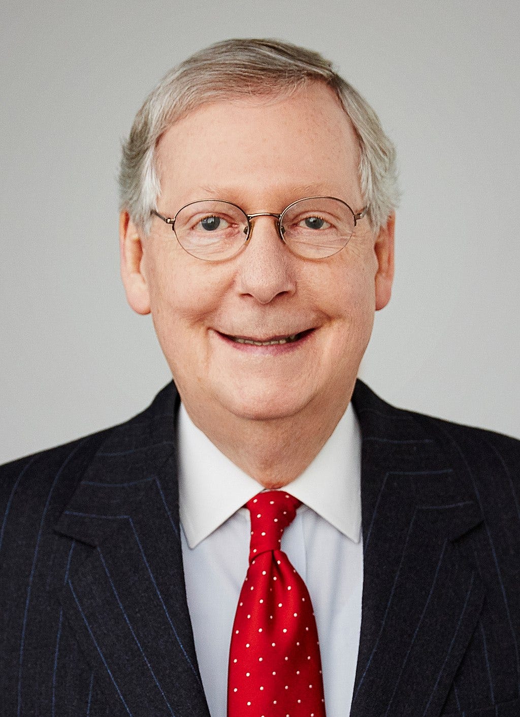 former Senate Majority leader Mitch McConnell, suit and red tie with white spots; glasses, thinning grey hair; famously, no chin