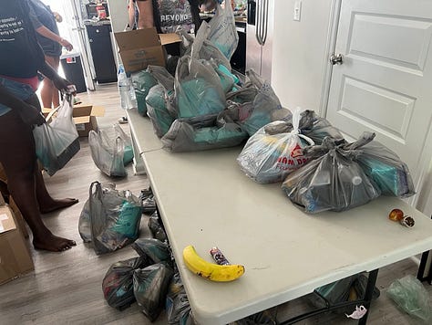 IMAGE 1: A white table with gray plastic bags full of dinner plates and safe sex kits. IMAGE 2: Stacks of black dinner plates and plastic bags on a wooden table. IMAGE 3: A green and yellow travel container full of safe sex kits. 