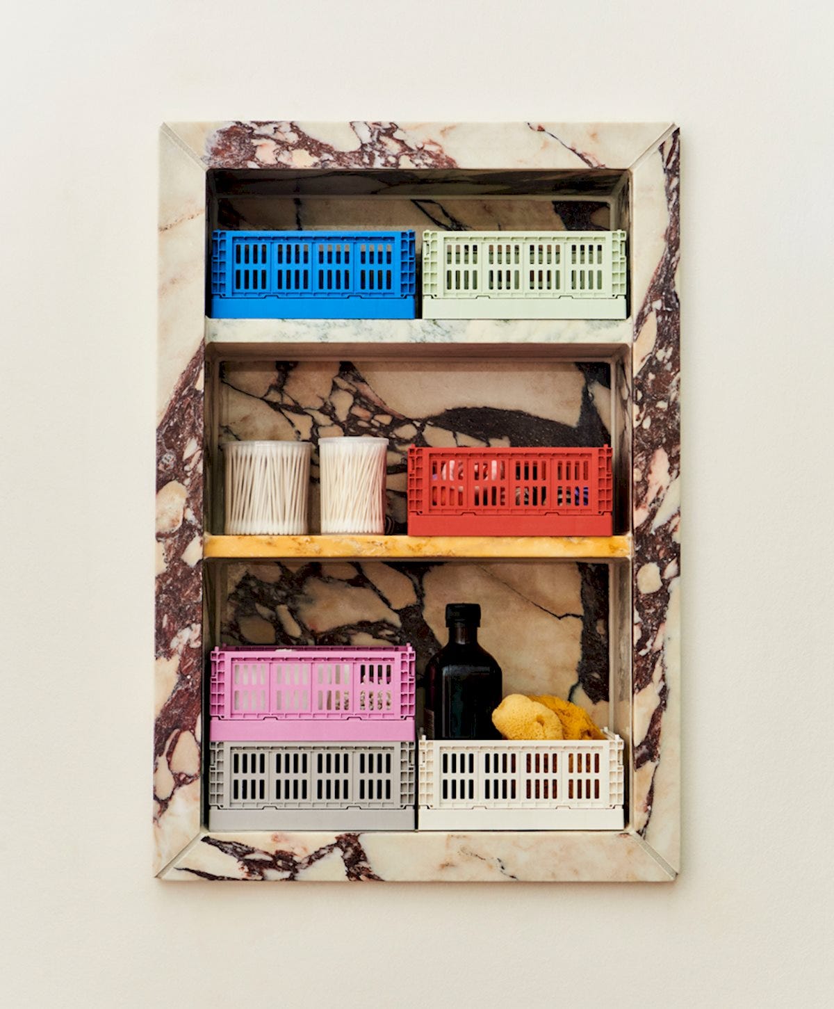 HAY Colour Crate Mini baskets in blue, sage, red, pink, and grey, arranged inside a recessed marble niche shelf with bathroom essentials.