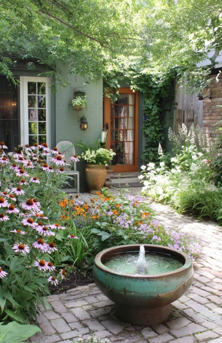 Small courtyard garden with layered planting, curved brick path, ceramic fountain, climbers, and flowering perennials creating a lush, intimate outdoor space
