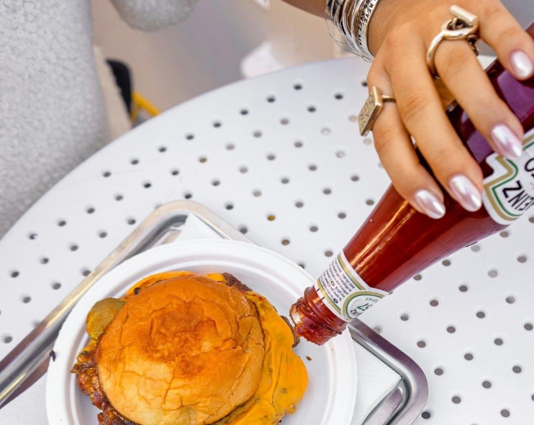 Hand adding ketchup to a double cheeseburger and fries. Hand adding ketchup to a double cheeseburger and fries.
