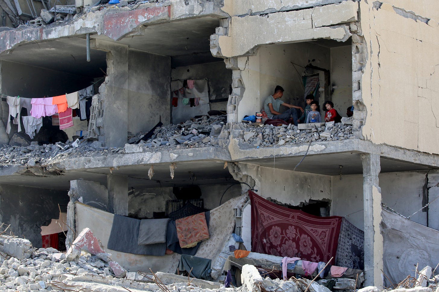 A Palestinian man and his children sit in a destroyed room of a building heavily damaged, apparently by an Israeli airstrike, in Rafah in the southern Gaza Strip on May 22, 2024 (Eyad AL-BABA / AFP)