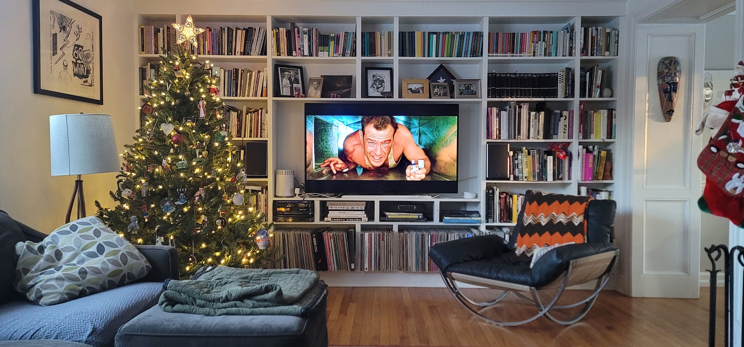 Photo of author's living room with a Christmas tree and a television with a shot of Die Hard paused, Bruce Willis' character crawling through a heat vent and with a lit Zippo lighter.