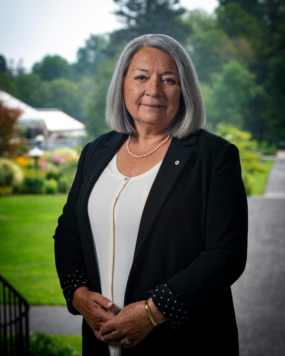 Official photo of Governor General Mary Simon. She is outdoors. The Rideau Hall gardens are visible in the background.