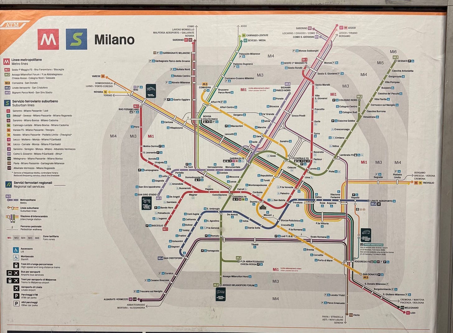 Milan ATM metro and suburban rail network map posted on a station wall, showing all lines including M1, M2, M3, M4, and regional rail connections across the greater Milan area