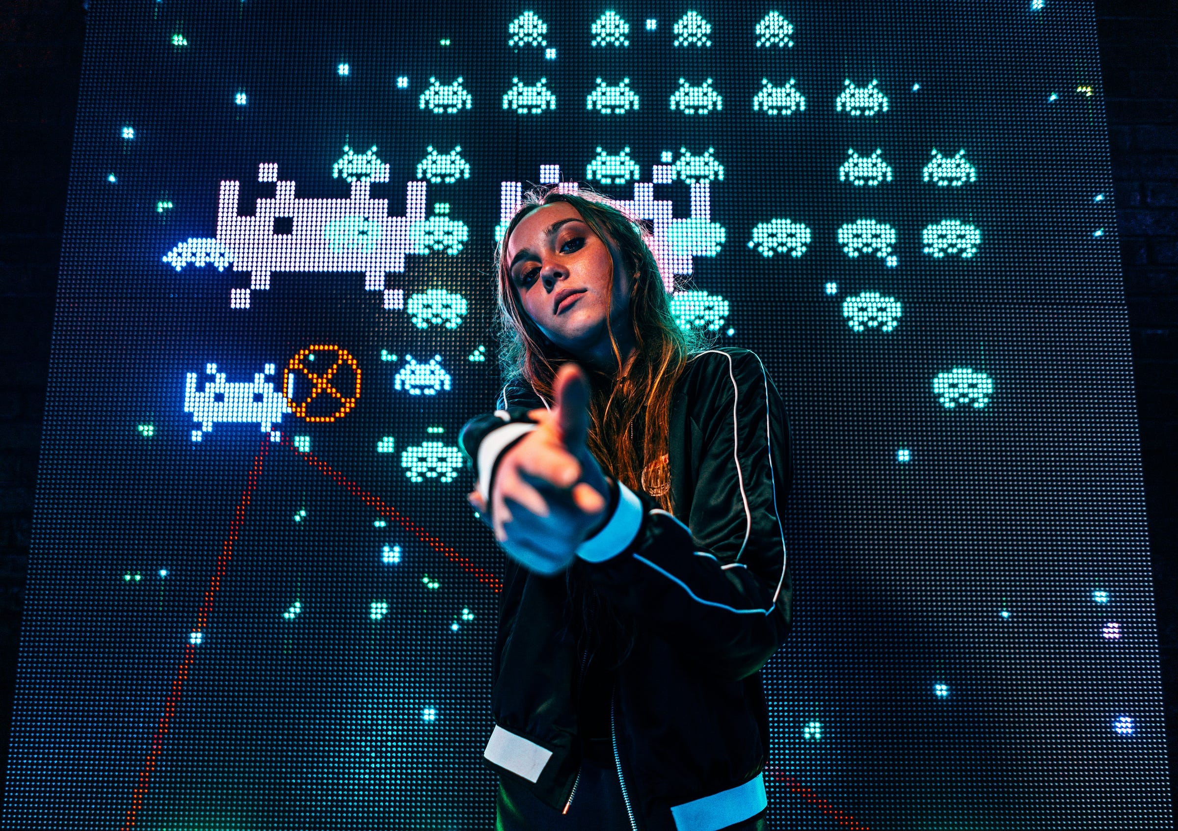 A girl simulating a gun with her hands, while standing in front of a big screen with the computer game Space Invaders A girl simulating a gun with her hands, while standing in front of a big screen with the computer game Space Invaders