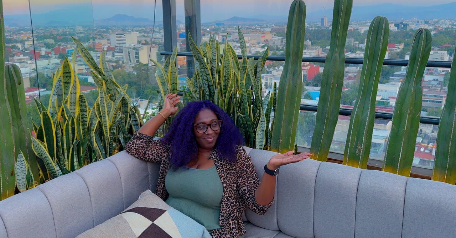 Black woman sitting on a sofa on a rooftop with the city skyline behind