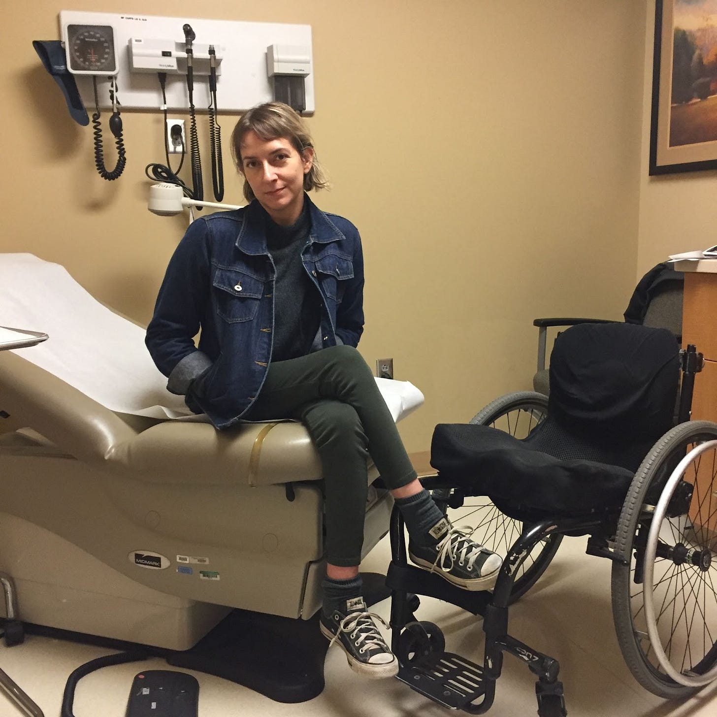 A mid-30s Rebekah sits on the edge of a hospital cot, the paper crumpled up beneath her. Her wheelchair sits beneath and to her left. She has her hands in the pockets of her denim jacket and looks straight into the camera, her face tired and maybe a little cynical. A mid-30s Rebekah sits on the edge of a hospital cot, the paper crumpled up beneath her. Her wheelchair sits beneath and to her left. She has her hands in the pockets of her denim jacket and looks straight into the camera, her face tired and maybe a little cynical.