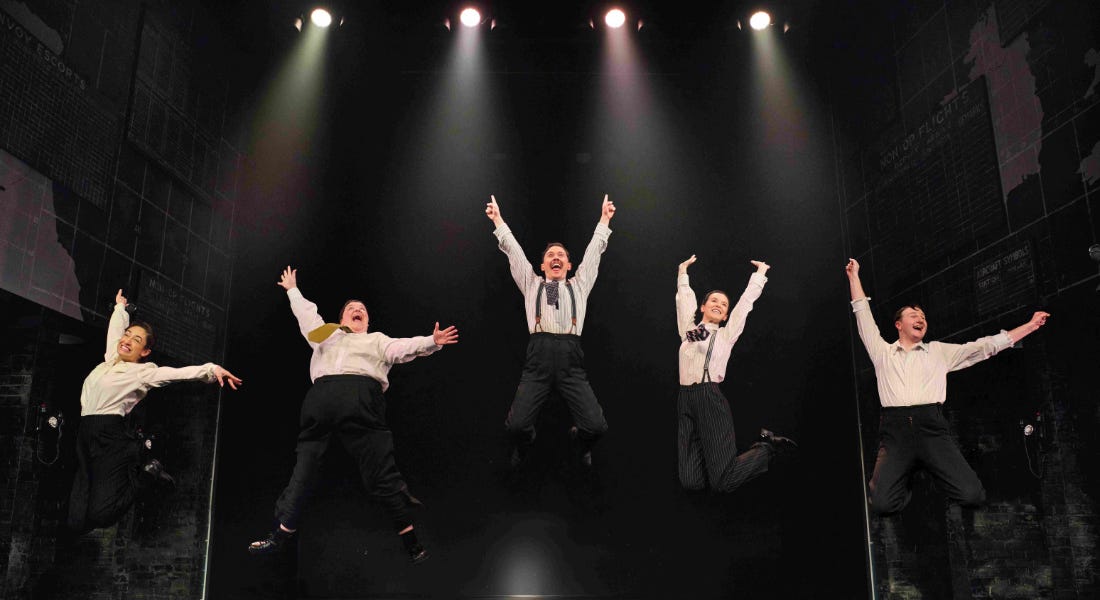 A group of five people jumping in the air, wearing shirts and black trousers, with a black background A group of five people jumping in the air, wearing shirts and black trousers, with a black background