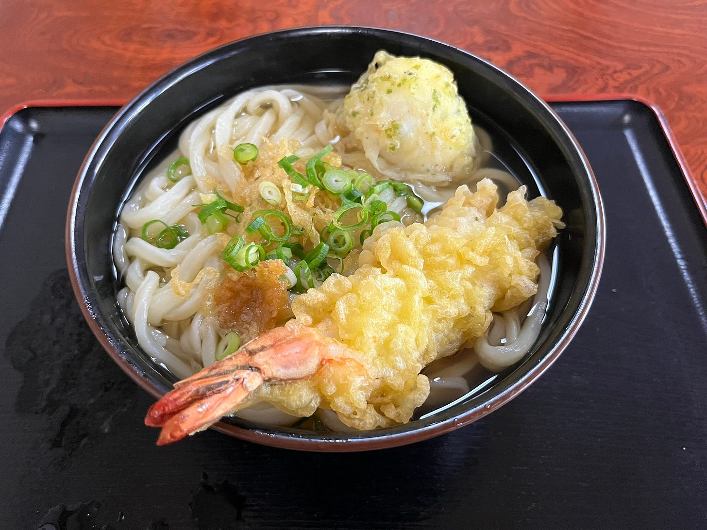 a bowl of hot udon in broth with an egg, scallions, tempura crumps, and shrimp tempura as toppings a bowl of hot udon in broth with an egg, scallions, tempura crumps, and shrimp tempura as toppings