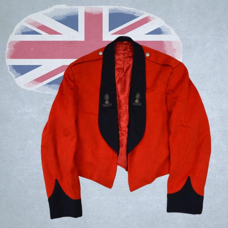 May include: A scarlet military jacket with black detailing on the lapels and cuffs. The jacket has two emblem pins and decorative buttons. A faded Union Jack flag is visible in the background.