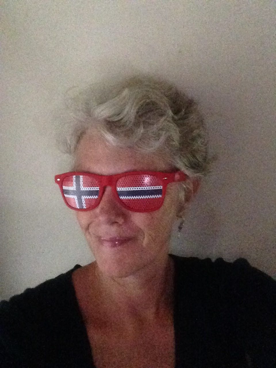 A woman with short, gray hair wearing glasses printed with the Norwegian flag.