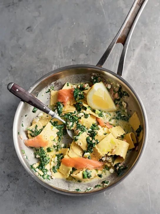 Smoked salmon pasta with spinach, spring onion, lemon in a stainless steel pan on a grey marbled surface