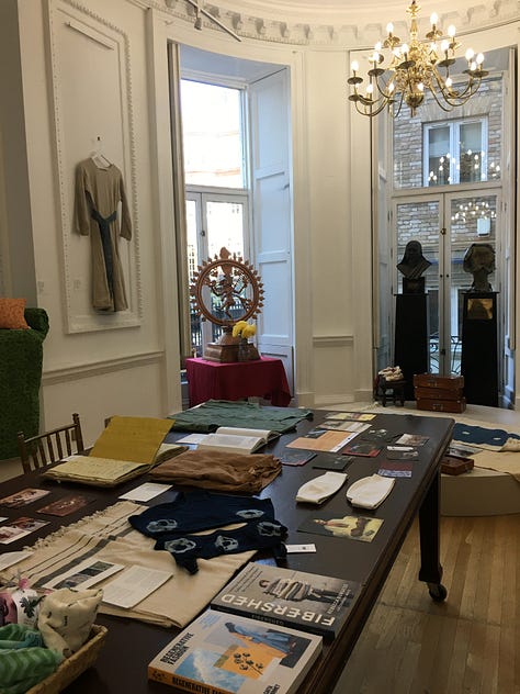 Views of the main exhibition space for Threads of Change at the Nehru Centre showing garments and fabric hanging on the walls with textile artefacts and books on the wooden table.