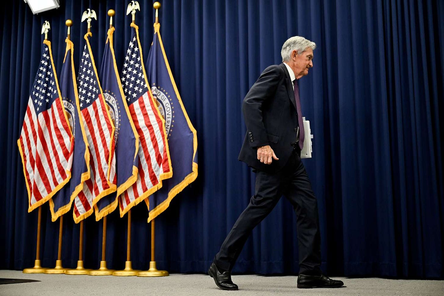Jerome Powell speaking at a Federal Reserve press conference in front of US flags, discussing interest rates and inflation outlook. Jerome Powell speaking at a Federal Reserve press conference in front of US flags, discussing interest rates and inflation outlook.