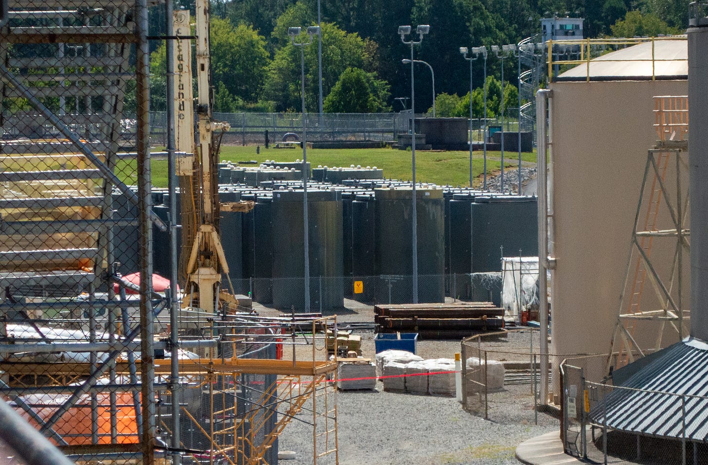 Rows of tall cylindrical dry cask containers store spent nuclear fuel outdoors behind fencing. Rows of tall cylindrical dry cask containers store spent nuclear fuel outdoors behind fencing.