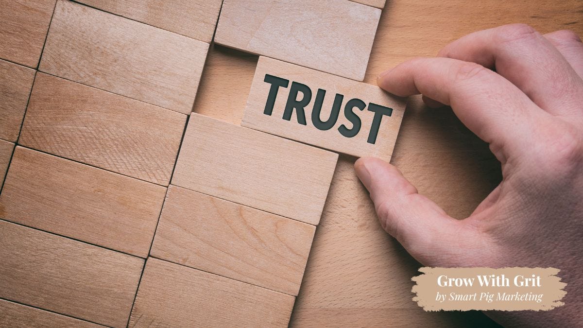 A hand places a wooden block labeled "Trust" into a partially completed wooden puzzle, symbolizing trust as the missing piece that completes a successful business and customer relationship. Grow With Grit by Smart Pig Marketing branding appears in the lower right corner.