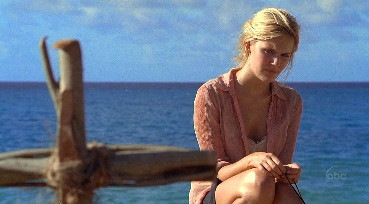 Shannon sits on the beach, looking at the two sticks that make the cross-shaped marker for Boone's grave.