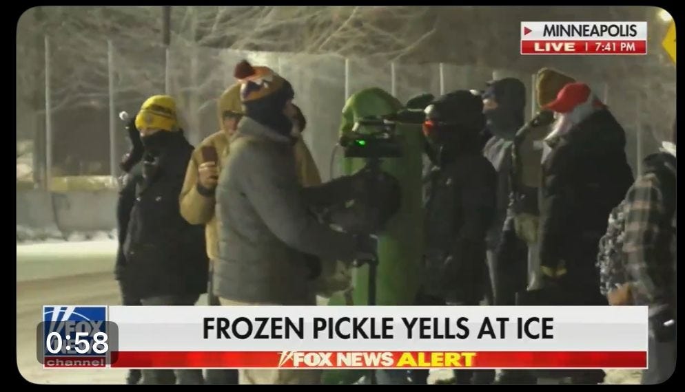 video screenshot showing a small crowd of very warmly-dressed protesters at night, one of whom is wearing a silly green pickle costume. Chyron reads 'FROZEN PICKLE YELLS AT ICE'