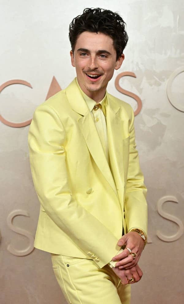 Timothée in a sleek suit, posing confidently with stylish rings and accessories at a public event